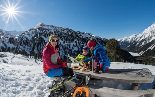 Tre persone fanno merenda all'aperto in inverno; due di loro studiano una cartina